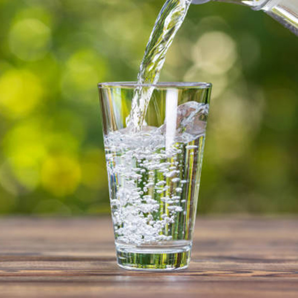 water from jug pouring into glass on wooden table outdoors